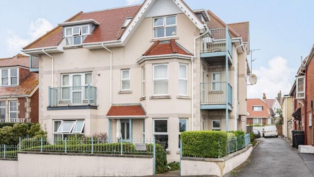 Een woonhuis met twee verdiepingen, een erker, een balkon en een kleine voortuin.