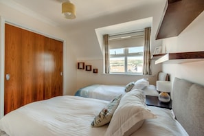 A hotel room with two beds, a window with curtains, a bedside table with a lamp, and a wooden wardrobe. - 3 Bed in Swanage (oc-83794) (Swanage)