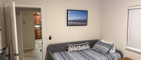 Un dormitorio con un sofá cama gris, ropa de cama a rayas, una pequeña mesa de madera y un cuadro en la pared.
