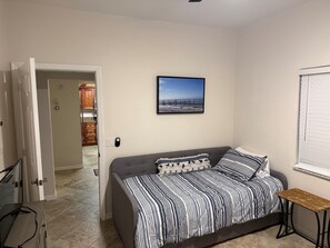 A bedroom with a gray sofa bed, striped bedding, a small wooden table, and a framed picture on the wall. - Casa Marina Condo with amenities (Fort Myers Beach)