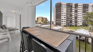En balkon med et bord og stole, der kigger ud over en skyskraber og et vandareal.