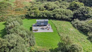 Een modern huis met een terras, omringd door weelderige begroeiing en heuvels.