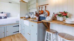 Een compacte keuken met een houten aanrechtblad, witte kastjes, en een kleine eethoek met krukken.