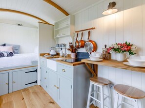 A compact kitchen with a wooden countertop, white cabinets, and a small dining area with stools. - 1 Bed in Boscastle (oc-84015) (Forrabury and Minster)