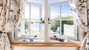 Een kamer met een groot raam, gordijnen en uitzicht op groen.