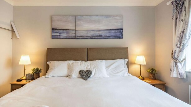 Ein Hotelzimmer mit einem großen Bett, zwei Nachttischlampen, einer herzförmigen Dekoration und einem Gemälde über dem Bett.