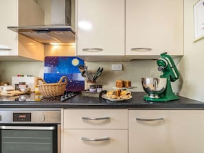 Eine Küche mit digitaler Uhr, einem grünen Standmixer und verschiedenen Backutensilien auf der Arbeitsfläche.