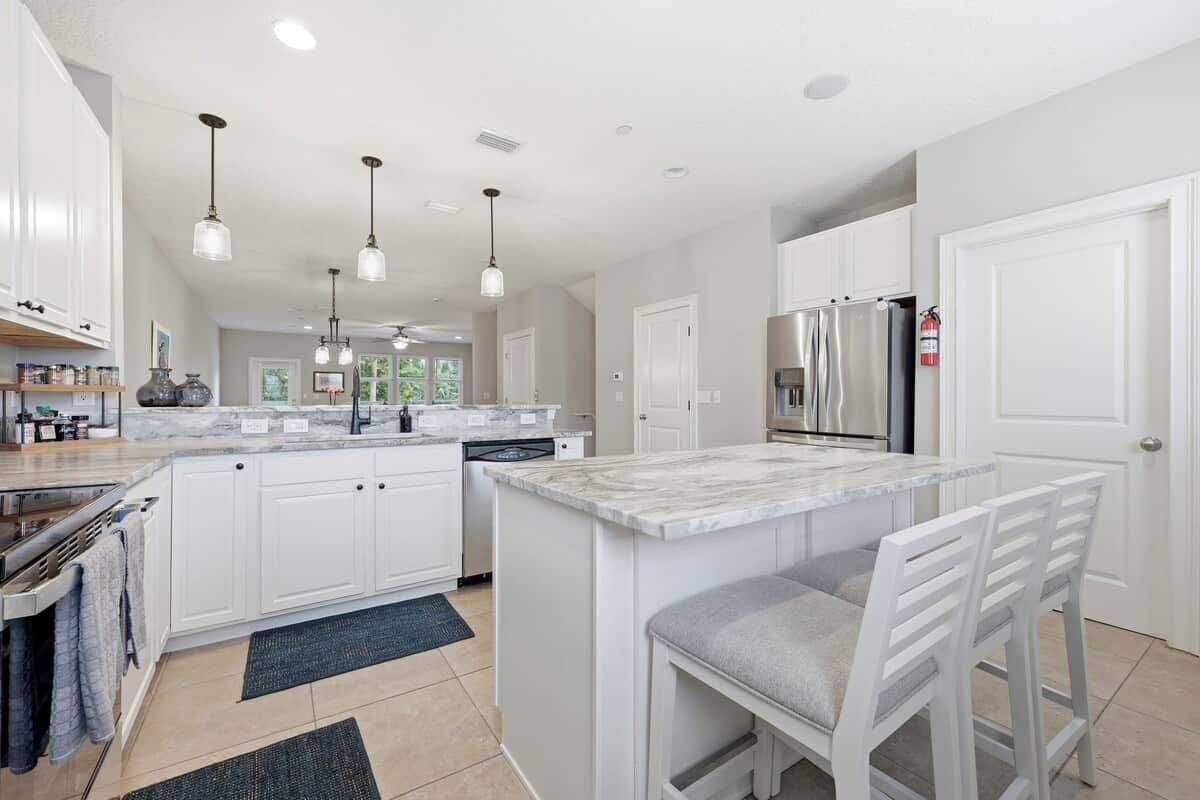 A modern kitchen with white cabinetry, a marble island, pendant lighting, and a stainless steel refrigerator.