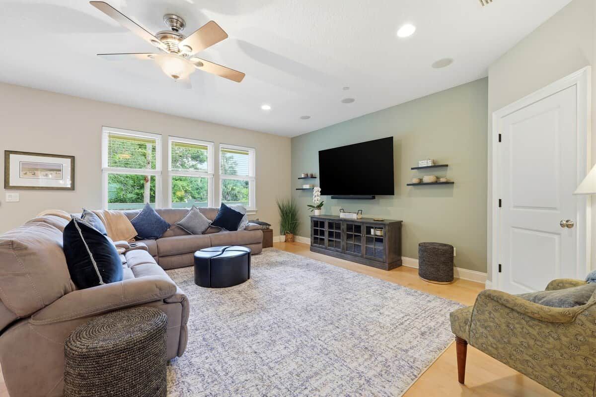 A living room with a sofa, ottoman, and a television on a stand.