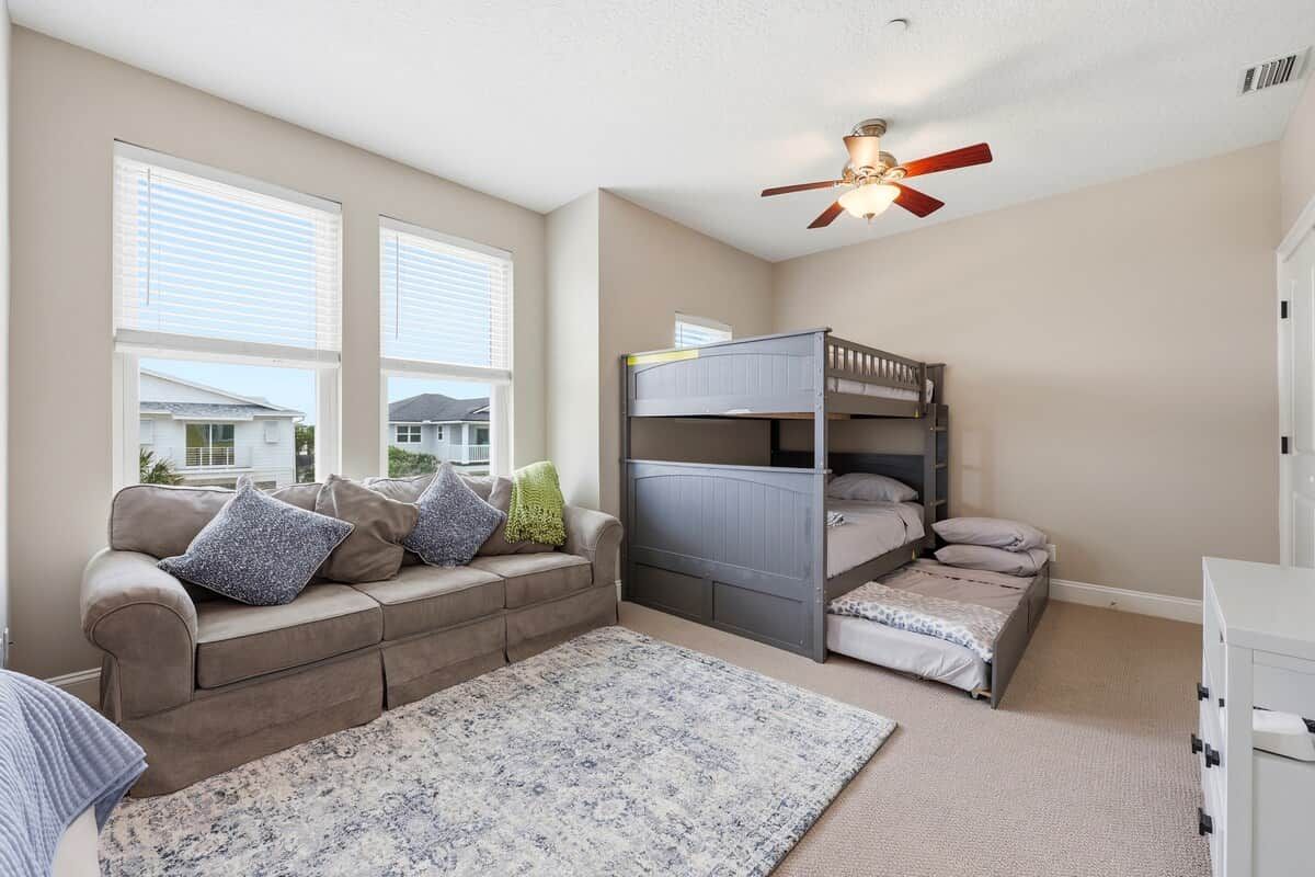 A bedroom with a bunk bed, a sofa, a large window, and a ceiling fan.