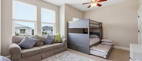 A bedroom with a bunk bed, a sofa, a large window, and a ceiling fan.