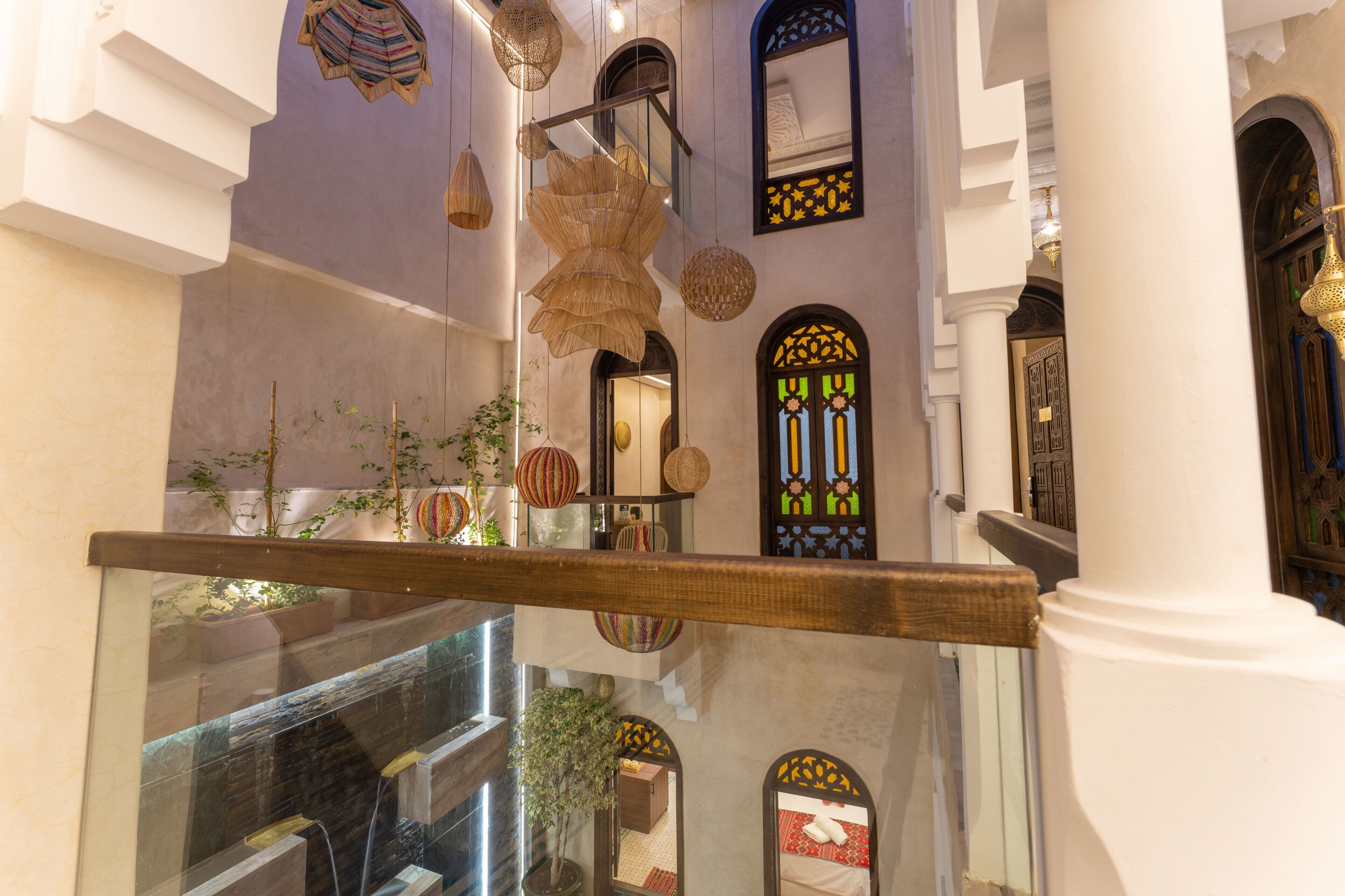 Un interior de varios niveles con una escalera, lámparas decorativas colgantes y vistas a una habitación con cama y ventana.