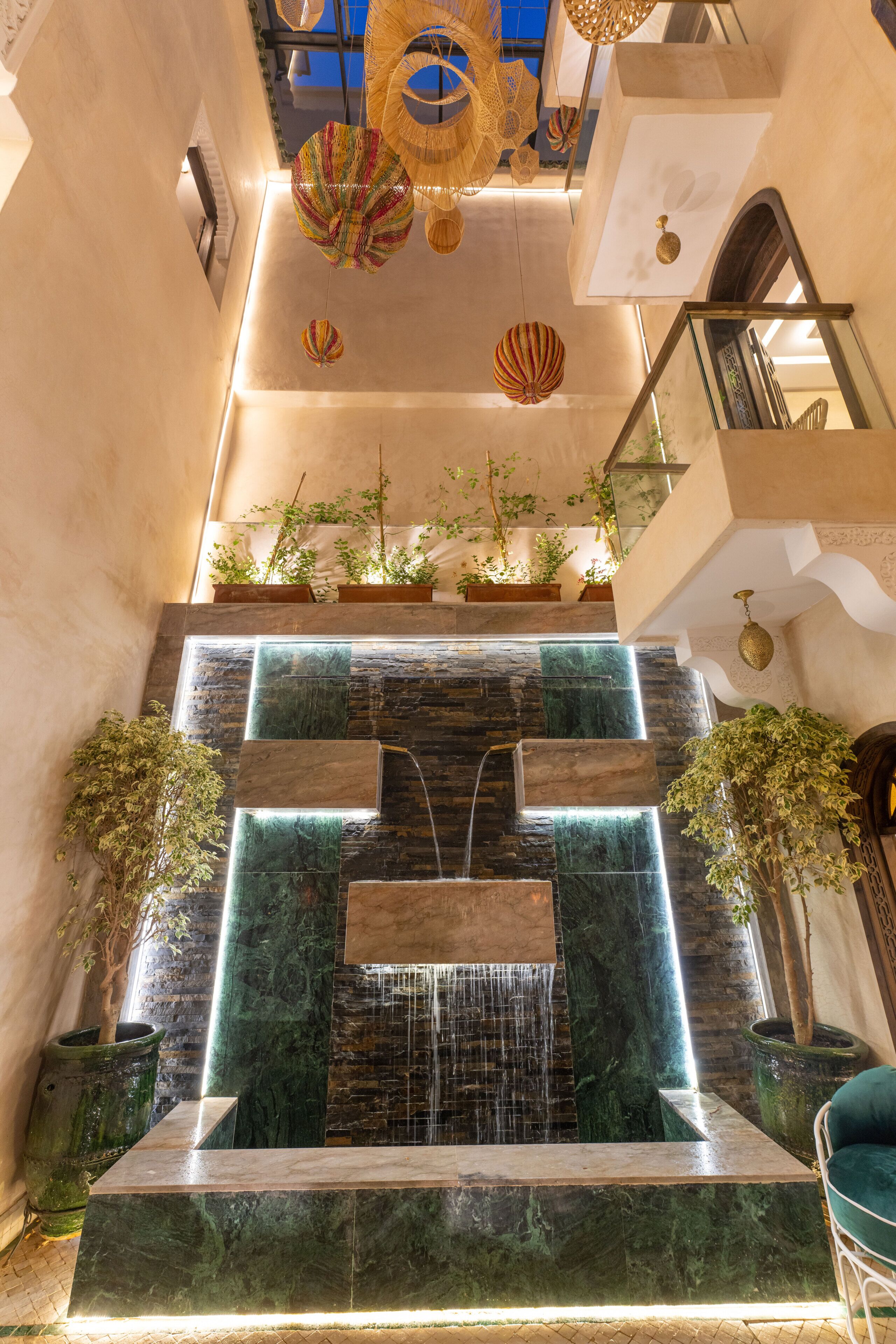 Un interior de varios niveles con una fuente central, plantas en macetas y una escalera.