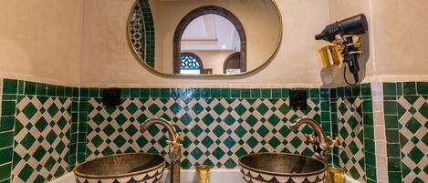 A bathroom with two large decorative bowls as sinks, a mirror, and a hairdryer mounted on the wall.