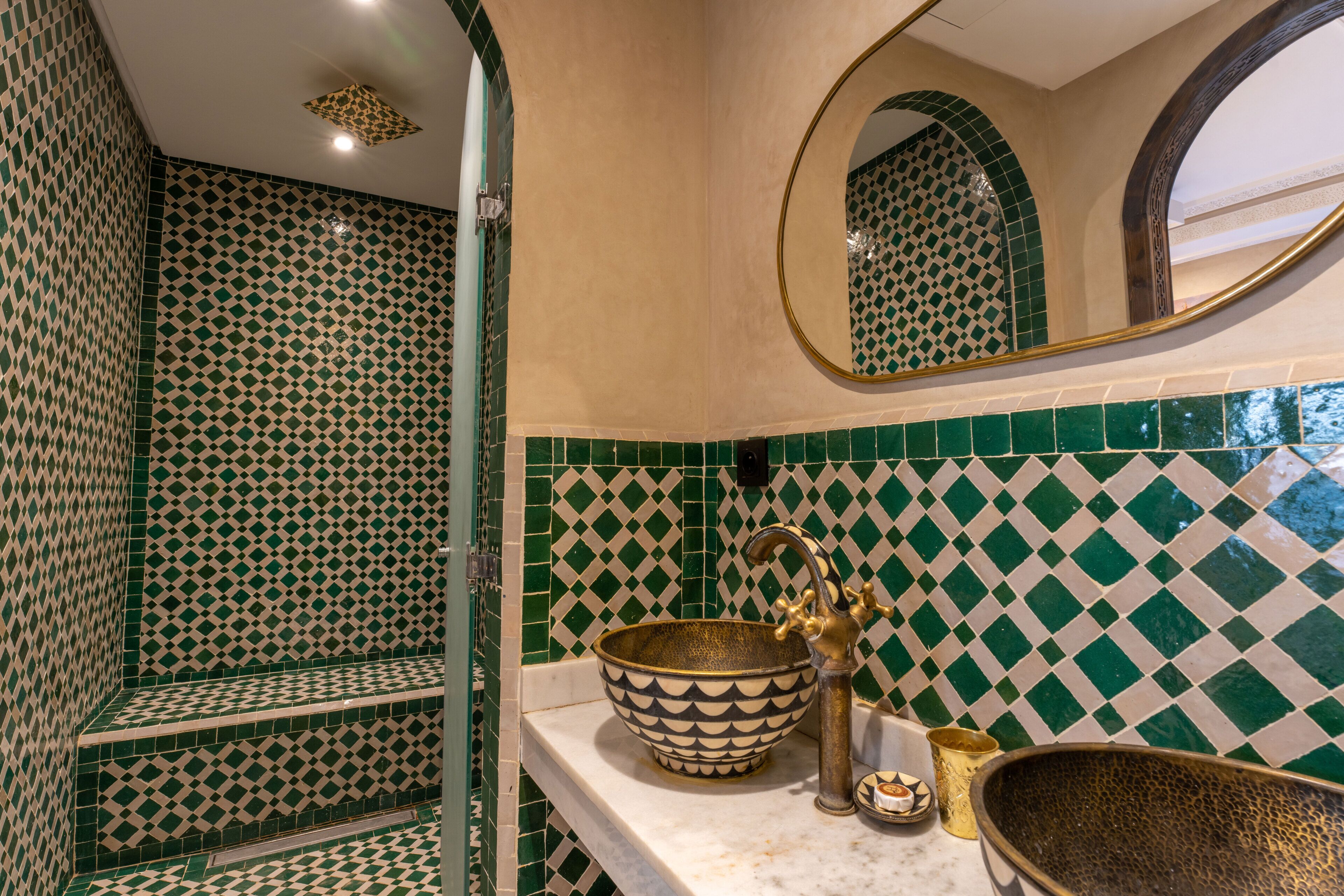 Un baño con pared de azulejos estampados, un lavabo con un cuenco decorativo y un espejo con un marco ornamentado.