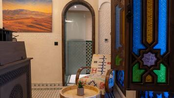 A room with a large painting, a wooden cabinet, a chair with a patterned cushion, and a decorative door.