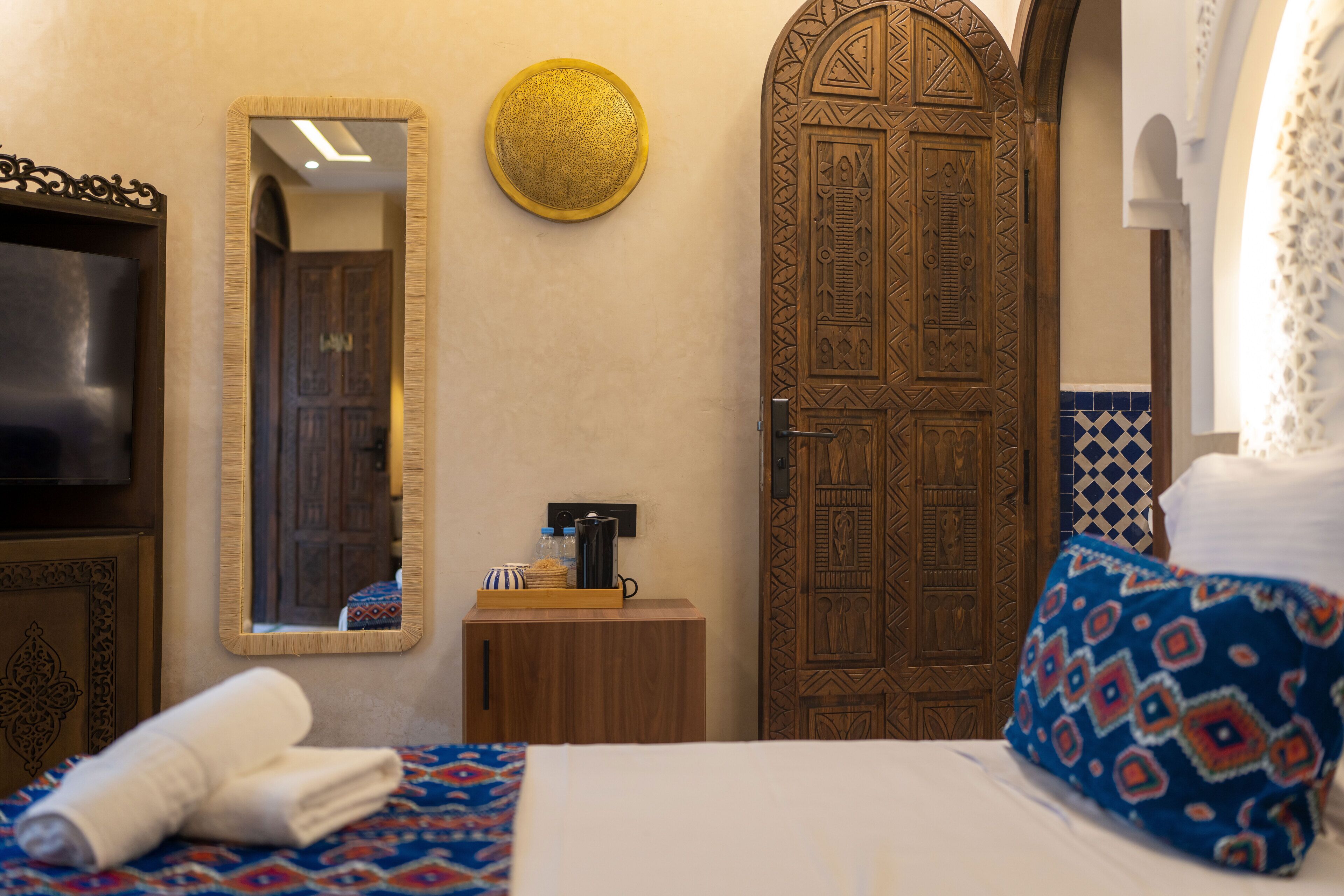 Habitación de hotel con cama, puerta de madera, espejo, pequeño armario de madera y televisor.