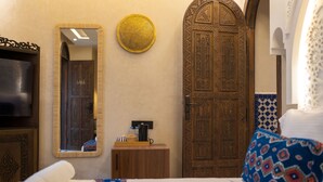 A hotel room with a bed, a wooden door, a mirror, a small wooden cabinet, and a television. - Riad Secret Mahjouba (Marrakech)