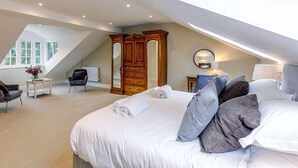 A bedroom with a large bed, a wooden wardrobe, a round mirror, and a small table with a vase of flowers. - 5 Bed in Harrogate (oc-83892) (Markington)