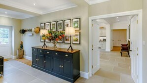 A spacious foyer with a dark wooden console, a wall-mounted lamp, and framed pictures. - 5 Bed in Harrogate (oc-83892) (Markington)