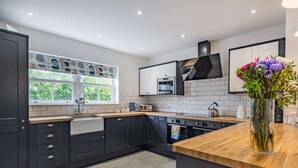 A modern kitchen with dark cabinetry, a wooden countertop, and a window with a view of greenery. - 3 Bed in Poulton-le-fylde (oc-83787) (Hambleton)