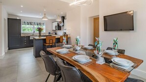 A modern kitchen with dark cabinets, a central island, and a dining area with a wooden table set for four. - 3 Bed in Poulton-le-fylde (oc-83787) (Hambleton)
