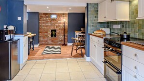 Una cocina compacta con pared de ladrillo, un área de comedor con sillas, un refrigerador, una estufa y un microondas.