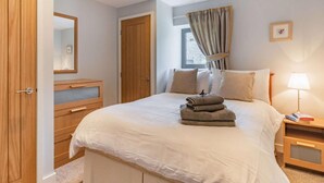 A bedroom with a bed, wooden wardrobe, bedside table, and a window with curtains. - 2 Bed in Cardigan (oc-83919) (Cilgerran)