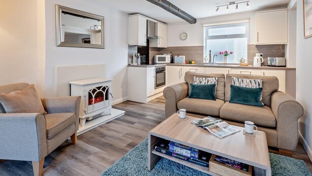 Ein gemütlicher Wohnbereich mit Sofa, Couchtisch, Kamin, Küchenzeile und großem Fenster.