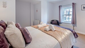 Ein Schlafzimmer mit einem Bett, Kissen, einem Sessel, einem Fenster mit Vorhängen und einer Heizung.