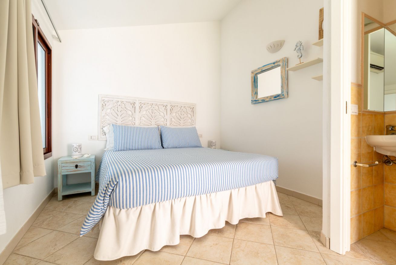 Un dormitorio con cama, mesita de noche, espejo y baño con lavamanos.