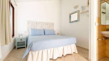 Un dormitorio con cama, mesita de noche, espejo y baño con lavamanos.