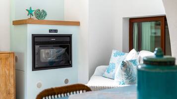 Una habitación con kitchenette, un armario de madera, un sofá con cojines estampados y una ventana con cortinas.