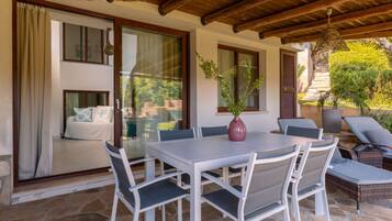Un espacio de comedor al aire libre con mesa y sillas, una planta en maceta y vistas a una casa con balcón.