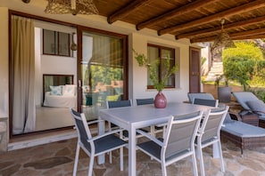 An outdoor dining area with a table and chairs, a potted plant, and a view of a house with a balcony. - Sa Barchitta in Villasimius in the bay of Porto Luna (Villasimius)