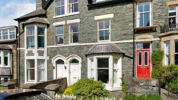 A multi-story stone building with a red door, white-framed windows, and a car parked in front. - 6 Bed in Keswick (oc-sz389) (Keswick)