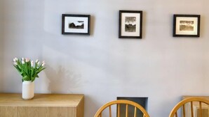A wall with three framed pictures, a white vase with green plants, and a wooden table with chairs. - 6 Bed in Keswick (oc-sz389) (Keswick)