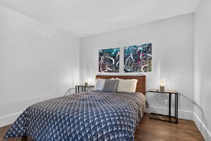 A bedroom with a bed, two bedside tables, and two wall-mounted paintings. - Charlevoix Cabin | Hot Tub |Pool Table | 22 Guests (Petite-Rivière-Saint-François)