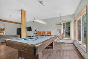 A modern living room with a pool table, a hammock, and a large window. - Charlevoix Cabin | Hot Tub |Pool Table | 22 Guests (Petite-Rivière-Saint-François)