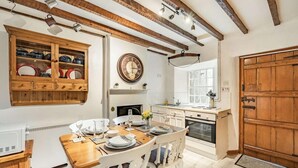 Una cocina con vigas de madera, un reloj, una mesa de comedor preparada para cuatro personas y una puerta de madera grande.