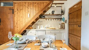 Comedor con mesa de madera preparada para cuatro personas, cocina al fondo y una escalera.