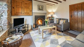 Una sala de estar acogedora con chimenea, pared de piedra, vigas de madera, un sofá, un televisor y una estantería.