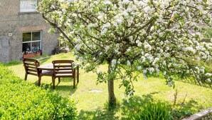 Ein Garten mit einem blühenden Baum, einer hölzernen Bank und einem Haus im Hintergrund.