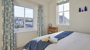 Ein Schlafzimmer mit Bett, Vorhängen, einem Fenster, einem Nachttisch und Blick auf Gebäude.