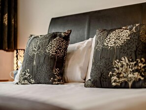Ein Bett mit zwei Zierkissen mit filigranen Mustern von Bäumen und Blättern.