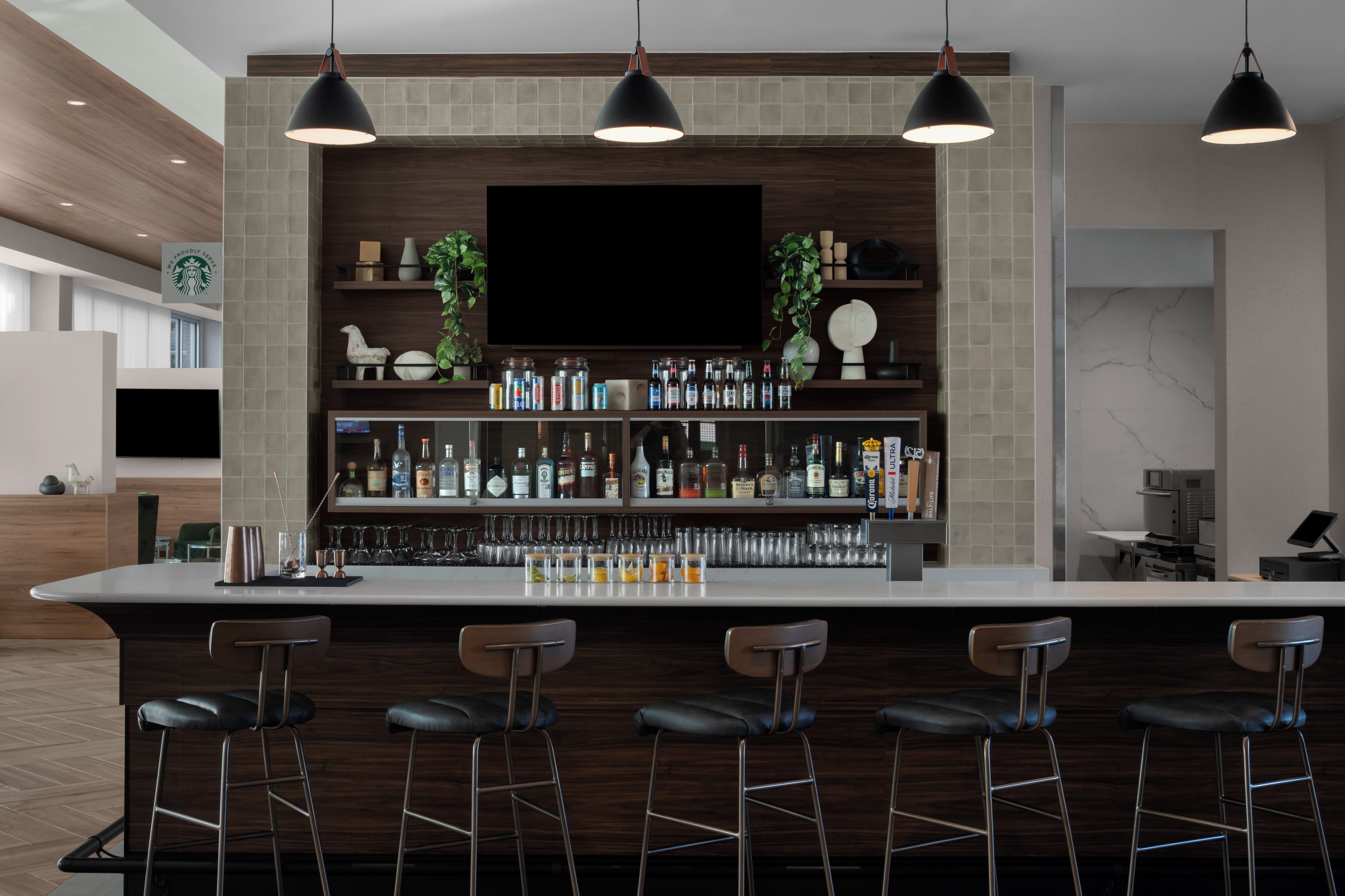 A modern bar area with a flat-screen TV, multiple liquor bottles, and bar stools.