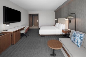 Habitación de hotel con cama, escritorio, silla, televisor, lámpara y una mesita.