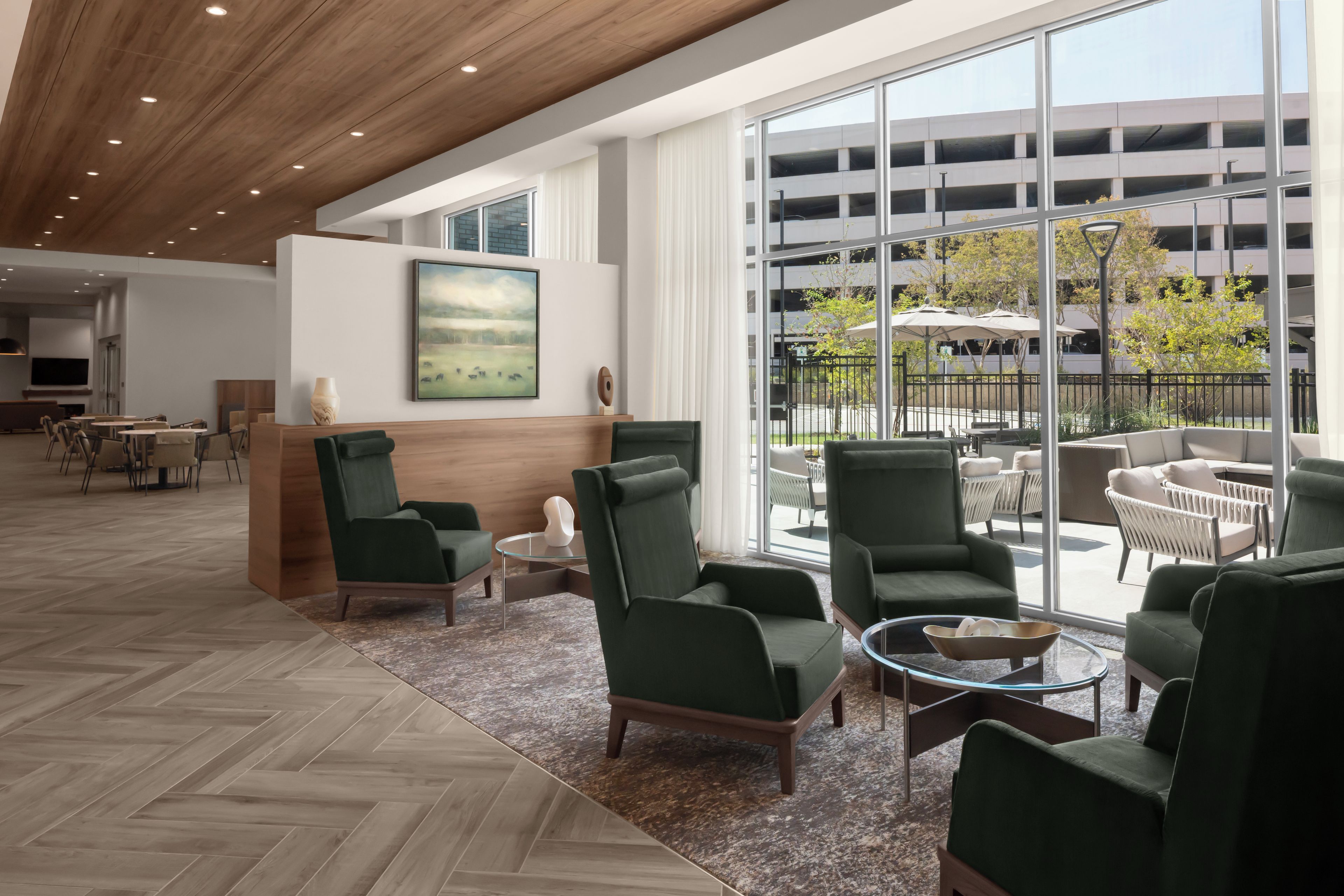 A spacious lobby with modern furniture, a large window offering a view of a parking garage, and a painting on the wall.