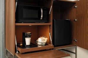 Una kitchenette equipada con microondas, refrigerador, cafetera y una cesta con toallas de papel.