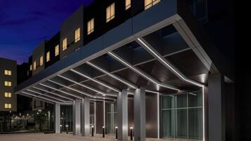 Una entrada de hotel moderna con un vestíbulo cubierto y columnas iluminadas.